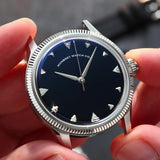 A close-up of a wristwatch with a silver-tone fluted bezel and a natural Onyx stone dial, held by two hands. Lab-grown diamond on dial.