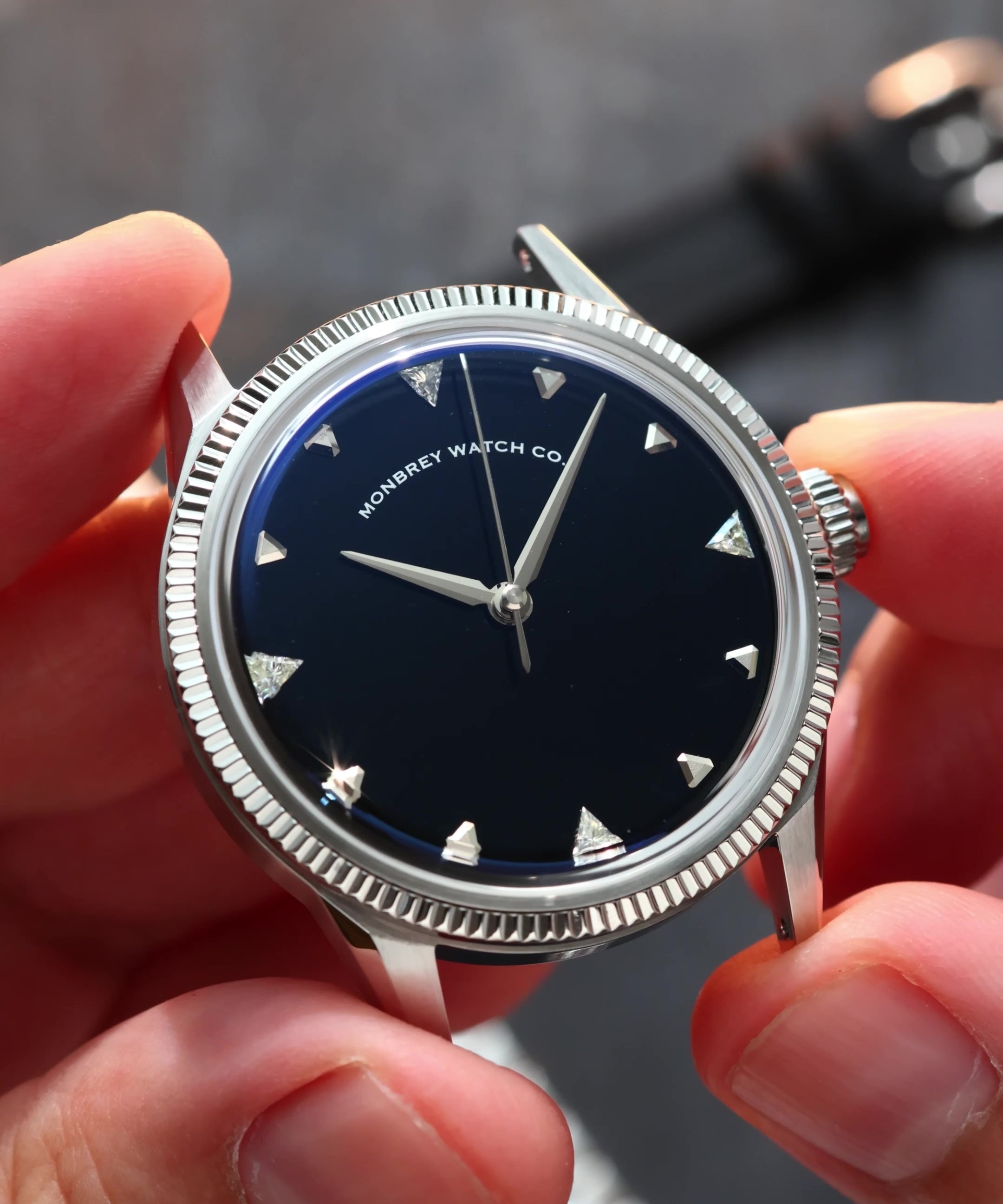 A close-up of a wristwatch with a silver-tone fluted bezel and a natural Onyx stone dial, held by two hands. Lab-grown diamond on dial.