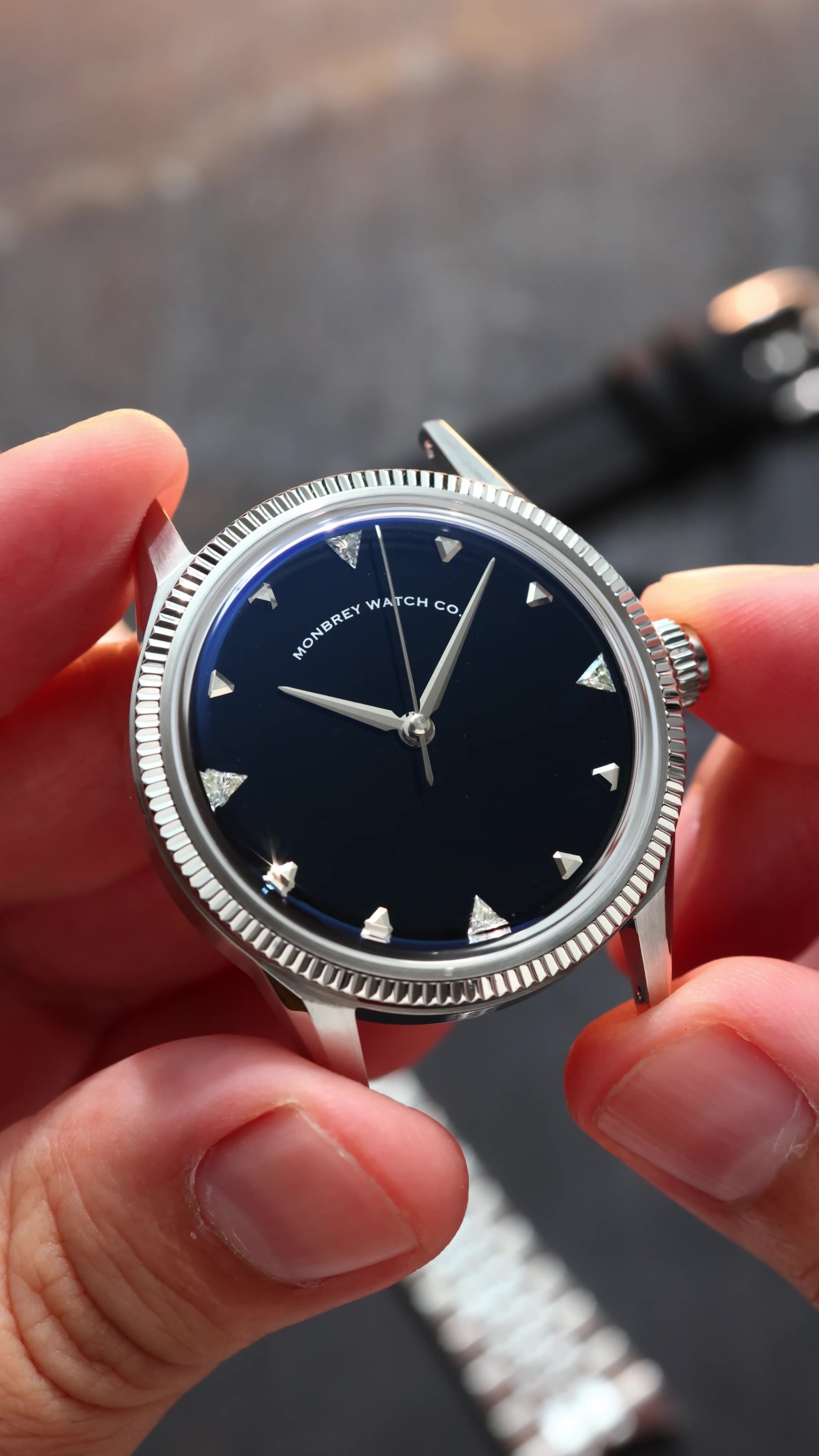 A close-up of a wristwatch with a silver-tone fluted bezel and a natural Onyx stone dial, held by two hands. Lab-grown diamond on dial.
