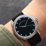 A wristwatch with a round silver-tone case and fluted bezel, and a natural Onyx stone dial, and a black croco leather strap, worn by a person in a casual setting. Lab-grown diamond on dial.