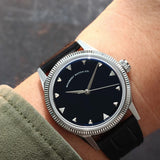 A wristwatch with a round silver-tone case and fluted bezel, and a natural Onyx stone dial, and a black croco leather strap, worn by a person in a casual setting. Lab-grown diamond on dial.