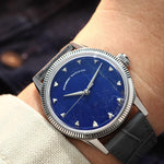 A close-up of a wrist wearing a vintage-style watch with a natural Sodalite stone dial, silver-tone case with fluted bezel, and dark gray leather strap.