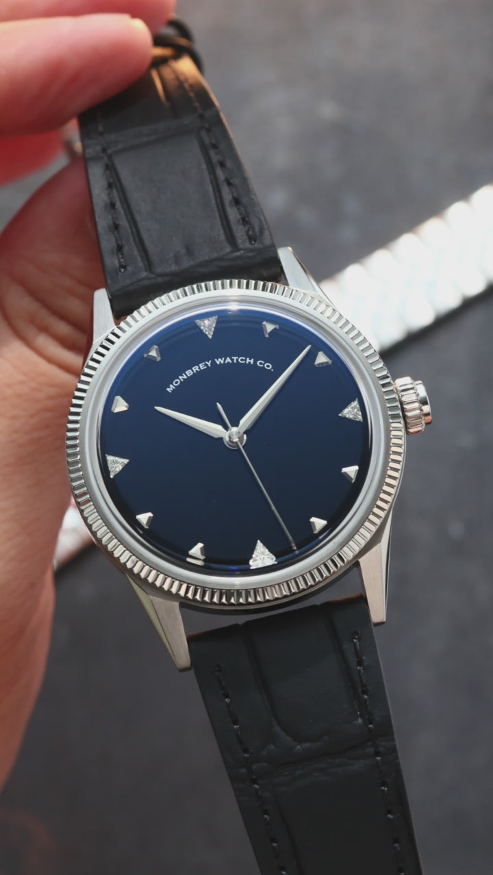 A wristwatch with a round silver-tone case and fluted bezel, a natural Onyx stone dial, and a black croco leather strap, styled on an dark textured surface background. Lab-grown diamond on dial.