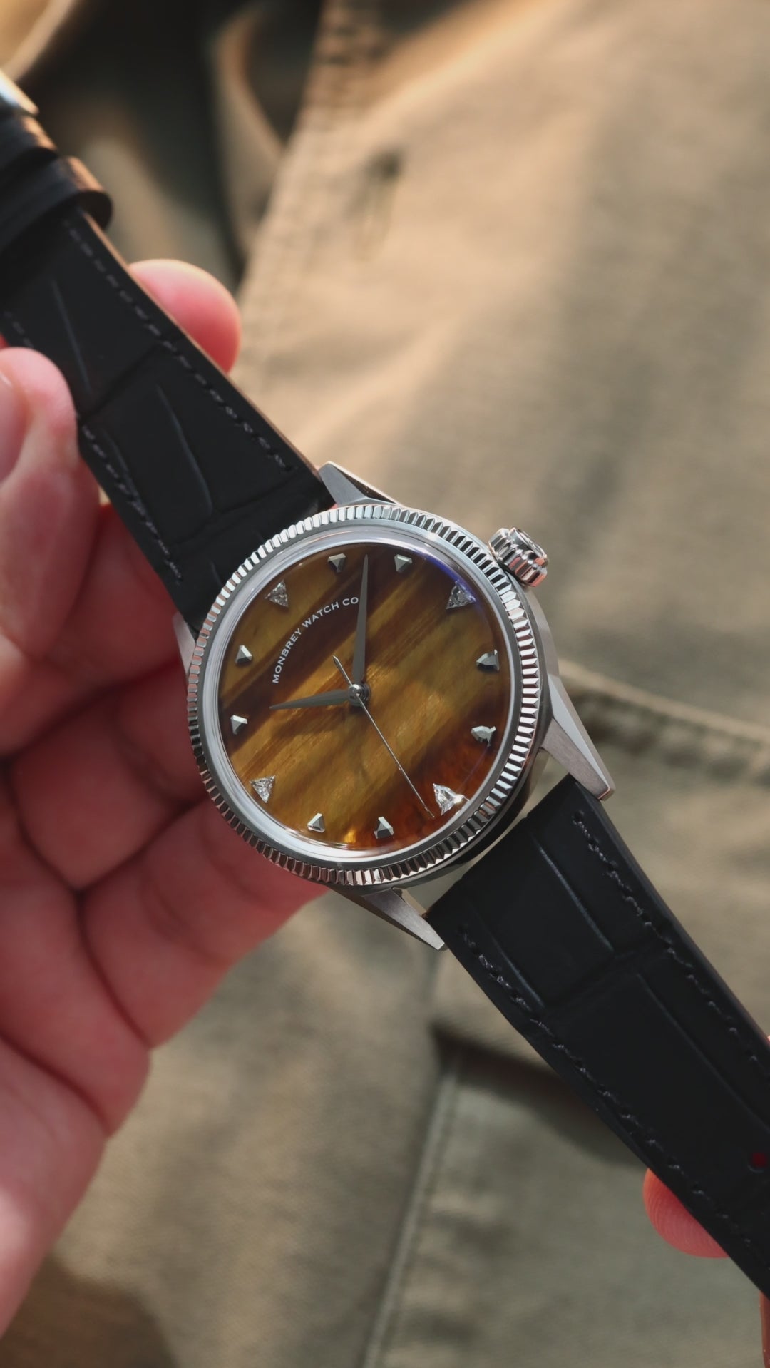 A wristwatch with a round silver-tone case, with a silver-tone fluted bezel, and a natural tiger eye stone dial, and a black croco leather strap. Lab-grown diamond on dial.