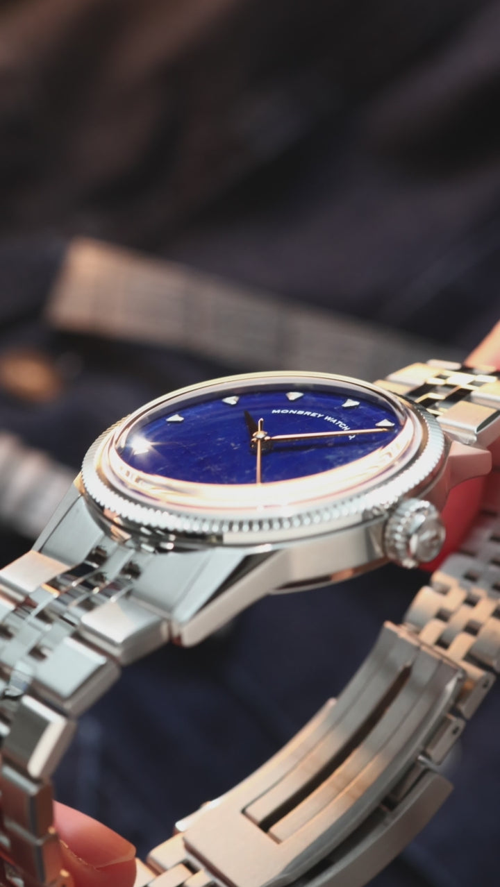 A close-up of a wrist wearing a vintage-style watch with a natural Sodalite stone dial, silver-tone case with fluted bezel, and silver jubilee bracelet.