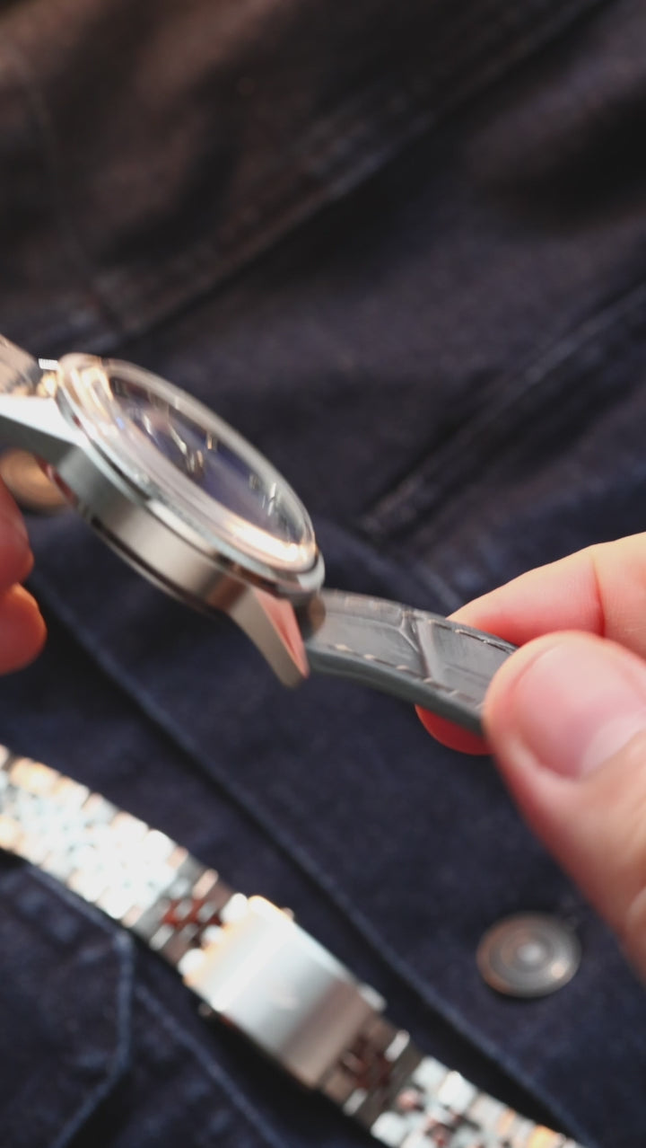 A close-up of a wrist wearing a vintage-style watch with a natural Sodalite stone dial, silver-tone case with fluted bezel, and dark gray leather strap.